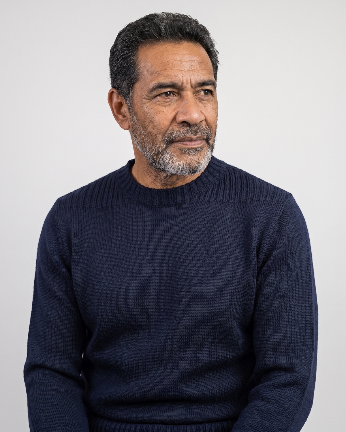 A man wearing a dark navy blue ribbed knit sweater, photographed against a plain light gray background.