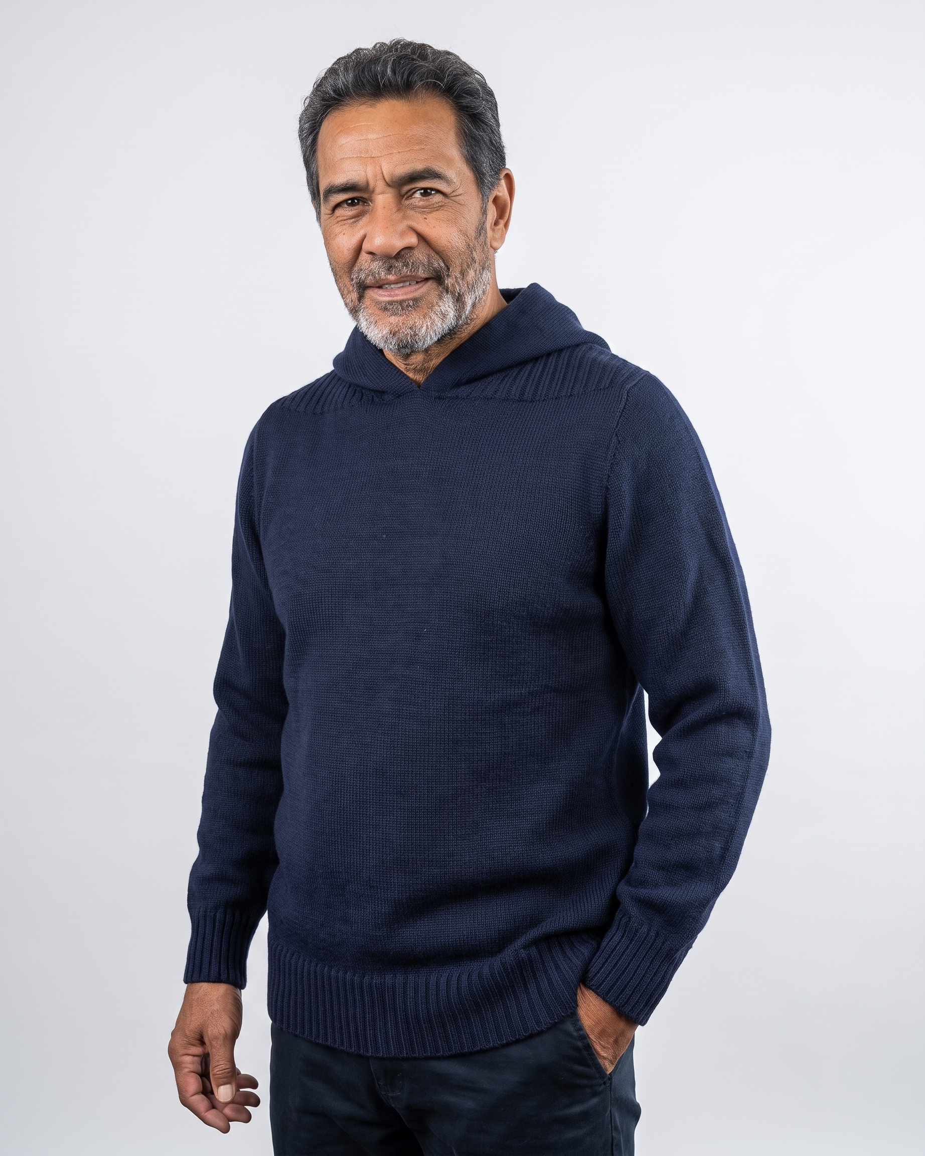 A man wearing a dark navy blue knit hooded sweater, standing against a light gray studio background.