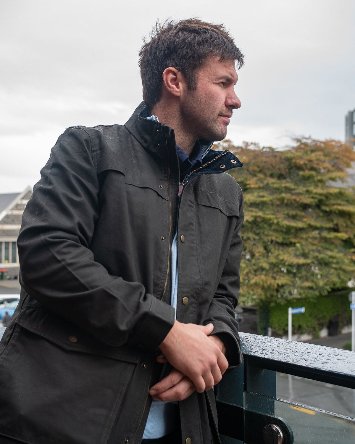 Dark haired man wearing a grey zip up jacket and jeans.