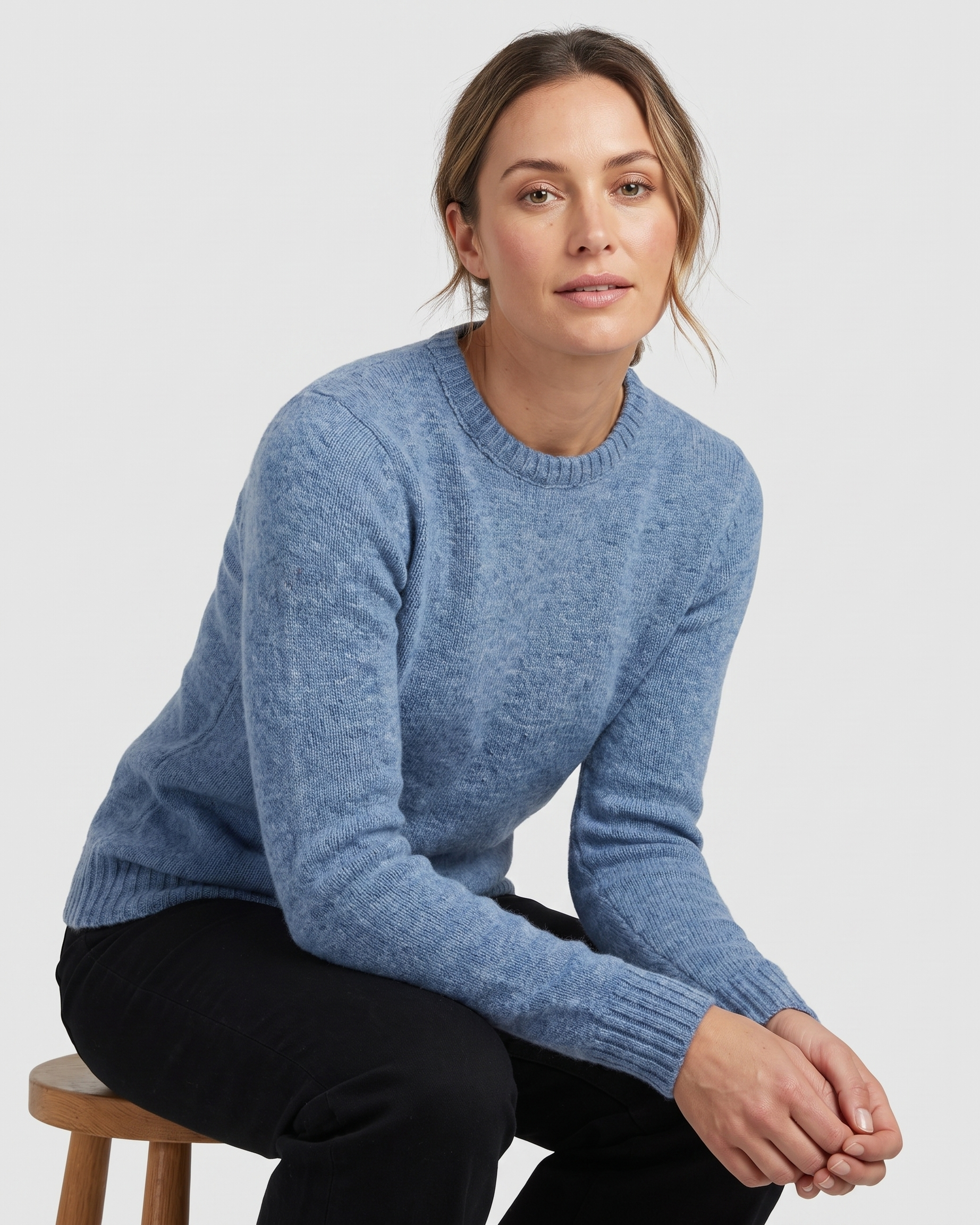 Woman wearing a blue sweater sitting on a stool against a white background
