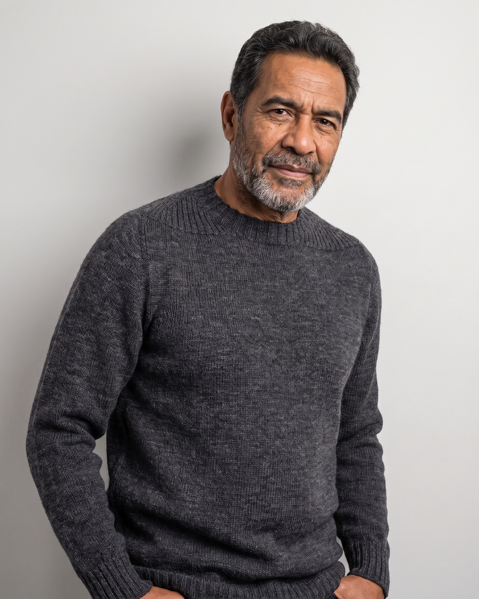 A man wearing a dark gray ribbed knit crewneck sweater, photographed against a plain light gray background.