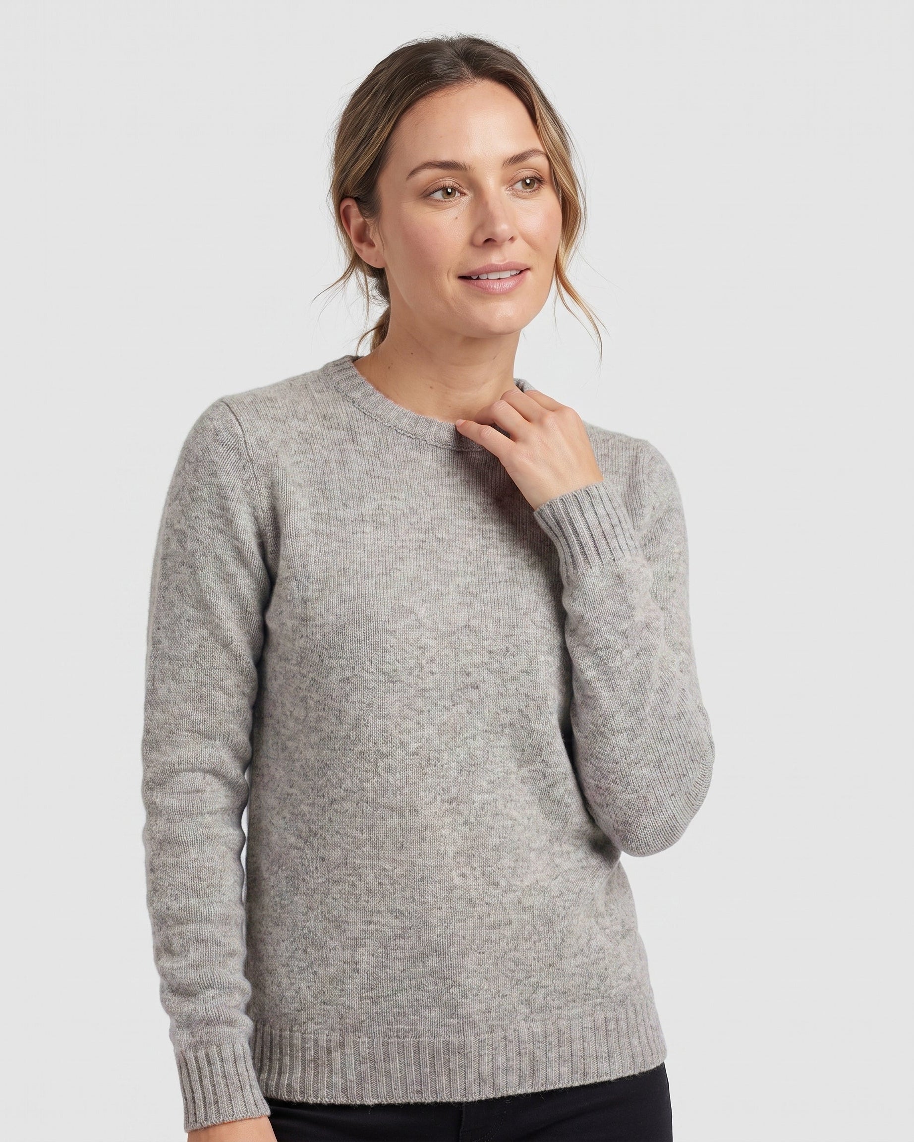 A woman wearing a light gray crewneck sweater, shown from the waist up against a solid light gray background.